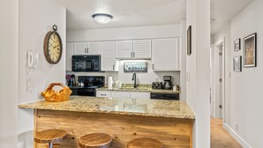 A modern kitchen with white cabinets, a granite countertop, and a bar area with stools.