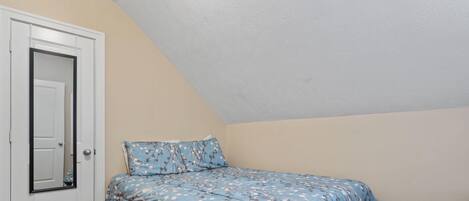A bedroom with a sloped ceiling, a bed with floral bedding, and a door with a mirror.