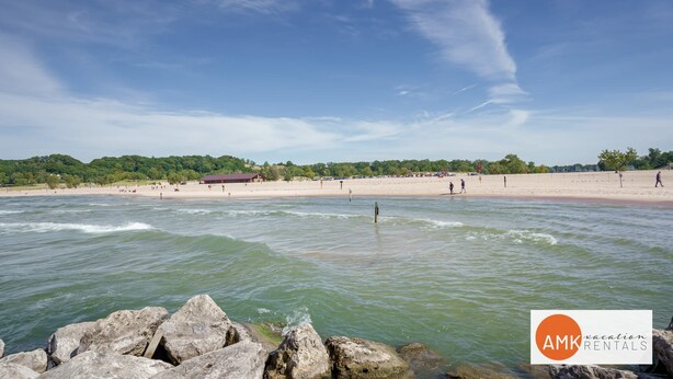 Ein Strand mit blauem Himmel, ruhigem Wasser und Gebäuden in der Ferne.