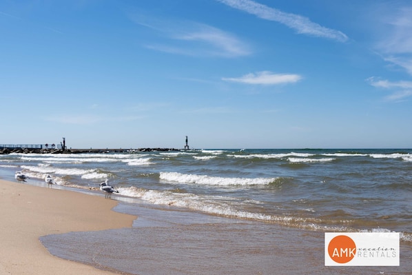 Een strand met golven, een vuurtoren en een pier.