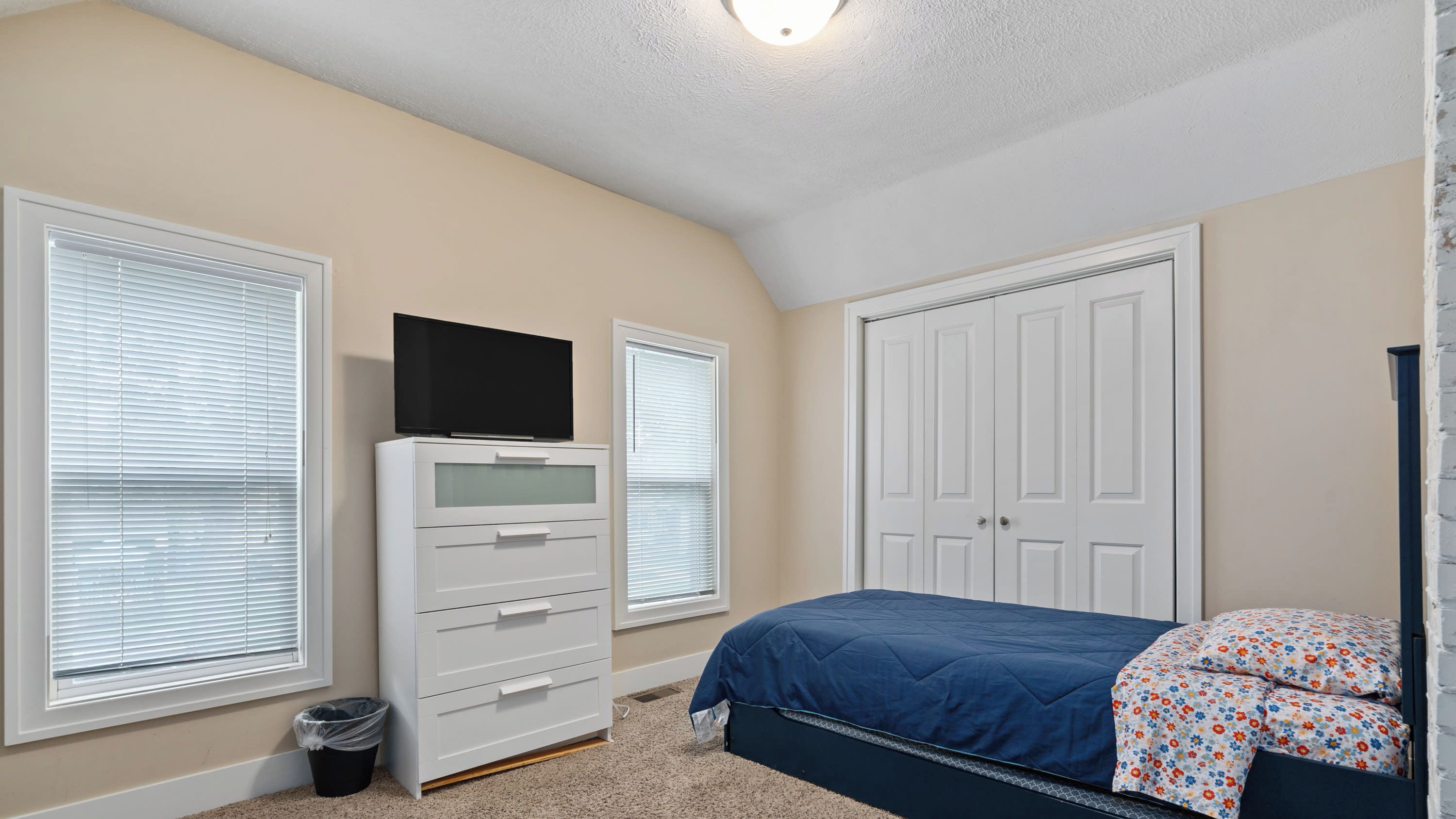 Een slaapkamer met een bed, een dressoir, een televisie en een kast.