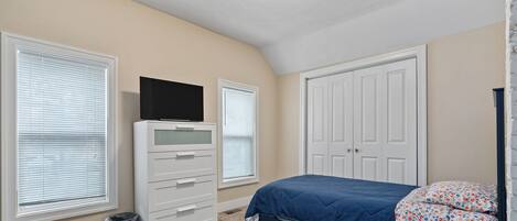 Een slaapkamer met een bed, een dressoir, een televisie en een kast.