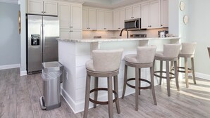 A modern kitchen with white cabinetry, stainless steel appliances, and a central island with bar stools. - 🌊☀Phoenix Orange Beach II 1005 - Beautiful 4BR Condo!☀🌊 (Orange Beach)