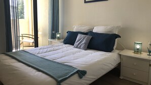 Een netjes opgemaakt bed met wit en blauw beddengoed, een groene plaid en een ingelijste foto aan de muur.