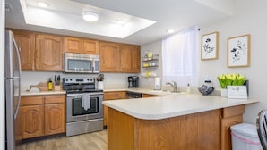 A modern kitchen with wooden cabinets, stainless steel appliances, a central island, and a window with curtains. - CASA AMARILLO - Anasazi Village - Updated Top Floor Unit (Phoenix)