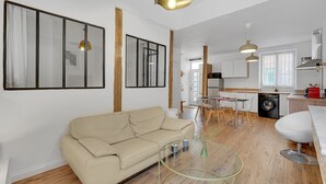 A modern living room with a beige sofa, a glass coffee table, and a dining area with a table and chairs. - LA PARENTHÈSE - Charmant T2 entièrement rénové (Toulouse)