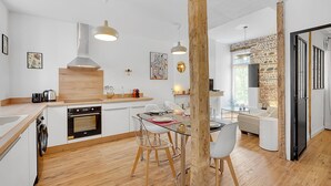 A modern kitchen with wooden countertops, a built-in oven, and a dining area with a glass table and chairs. - LA PARENTHÈSE - Charmant T2 entièrement rénové (Toulouse)