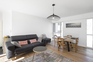 Ein modernes Wohnzimmer mit einer schwarzen Couch, einem kleinen runden Tisch und einem Essbereich mit Holzsesseln und einem Tisch.