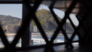 A view of a coastal area with buildings, a hill, and a beach through a window with a geometric pattern. - Always Easy I Sagües (San Sebastián/Donostia)
