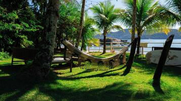 Relax in a serene hammock suspended between trees, overlooking a tranquil body of water surrounded by lush greenery.