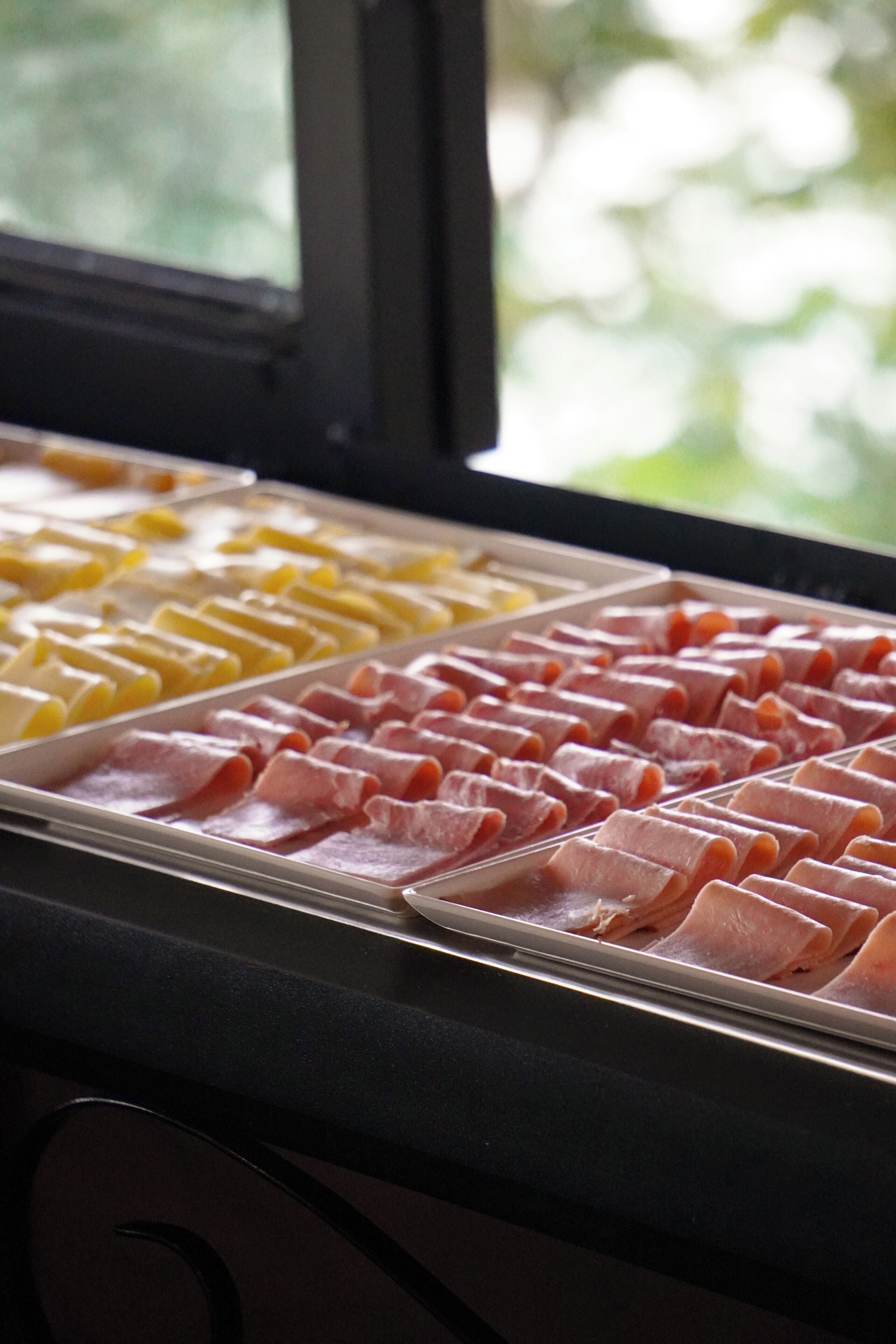 Un bufé con distintos alimentos, incluyendo carnes y quesos en porciones.