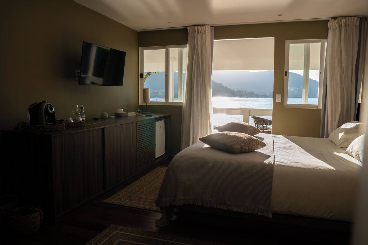 Habitació d'hotel amb un llit, escriptori amb televisió de pantalla plana, finestra amb vista al mar i un balcó.