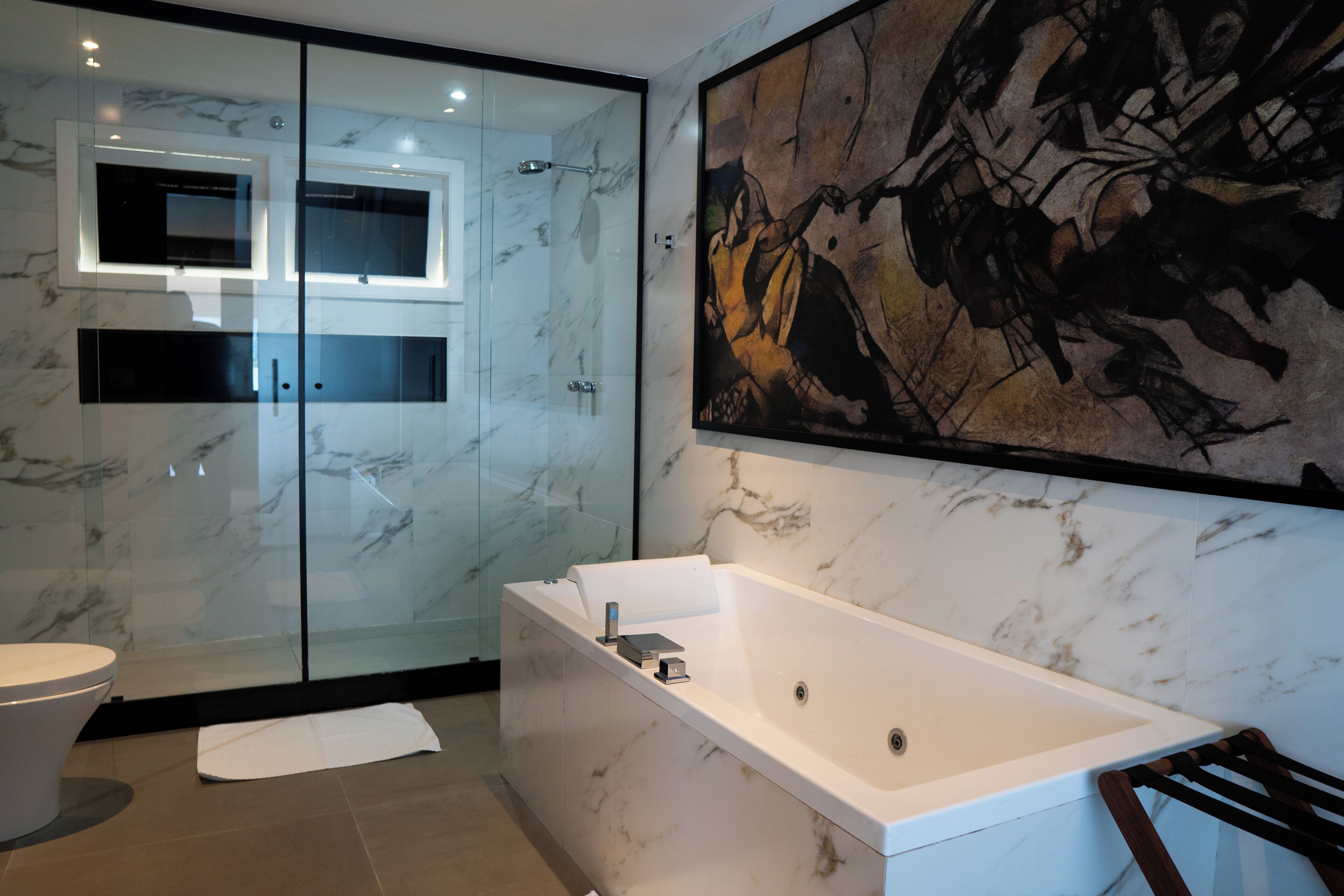 Un baño moderno con cabina de ducha de vidrio, una bañera blanca y un cuadro abstracto grande en la pared.