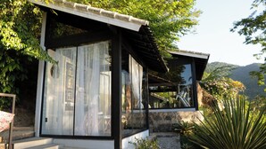 A modern house with a stone foundation, large windows, and a wooden staircase leading to the entrance. -  Pousada Papiro Boutique (Angra dos Reis)
