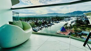 A modern room with a curved white chair, a glass balcony, and a view of a marina and cityscape. - Entire 2 Bedroom 2 Bath Marina Vallarta condo with insane view  (Puerto Vallarta)