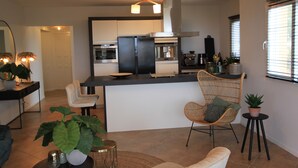 A modern kitchen with a central island, a dining area with a chair, and a living space with a sofa and a coffee table.
