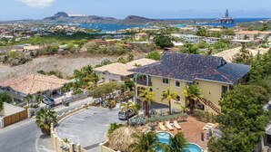 A coastal property with a swimming pool, a parking area, and a view of the sea and mountains.