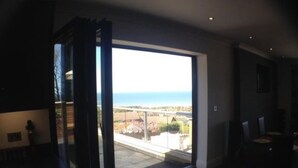 Ein Zimmer mit einer großen Schiebeglasdoor zum Balkon mit Blick auf das Meer und Gebäude.