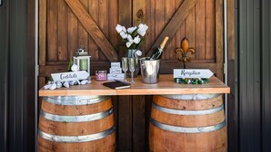 Un área de recepción con una mesa de madera, dos barriles de madera, un letrero que dice 'Cocktails' y un letrero que dice 'Recepción'.