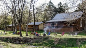 Un lodge rústico con techo de metal, mobiliario exterior y un pequeño estanque.