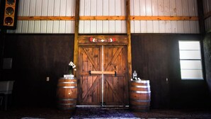 Interior rústico de un granero con vigas de madera, una puerta de madera grande y dos barriles.