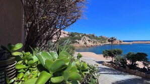 Une vue sur la côte, avec un ciel dégagé, une côte rocheuse et un bâtiment doté d’un balcon donnant sur la mer.