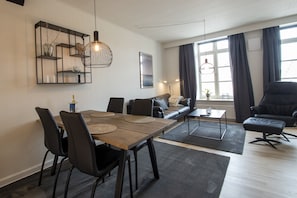 Een moderne woonkamer met een eethoek, met een houten tafel, zwarte stoelen, een bank en een salontafel.