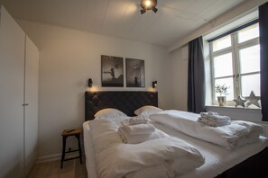 Een hotelkamer met een groot bed, twee wandluidsprekers, een plafondventilator en kunst aan de muur.