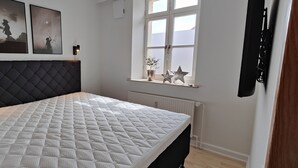 Un dormitorio con una cama grande, una ventana con vistas y dos marcos con cuadros colgados en la pared.