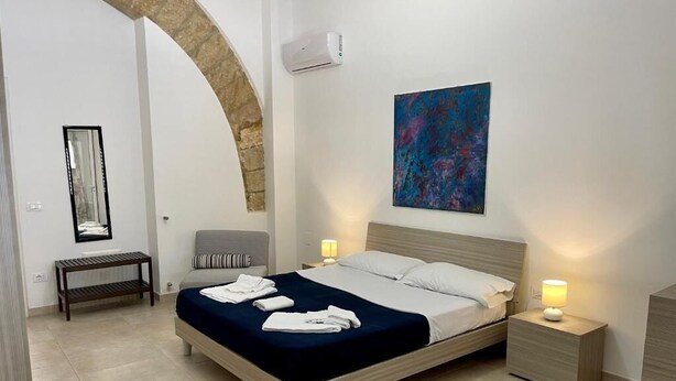 A modern bedroom with a bed, bedside tables, a bench, and a large abstract painting on the wall. - Jade House in the CENTER a stone's throw from the sea (Castellammare del Golfo)