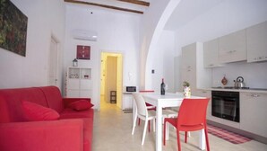 A compact living space with a red sofa, a dining table with chairs, a kitchenette, and a small hallway. - Jade House in the CENTER a stone's throw from the sea (Castellammare del Golfo)