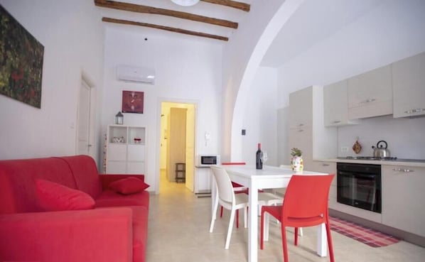A compact living space with a red sofa, a dining table with chairs, a kitchenette, and a small hallway.