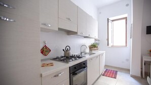 A modern kitchen with white cabinets, a gas stove, and a window providing natural light. - Jade House in the CENTER a stone's throw from the sea (Castellammare del Golfo)