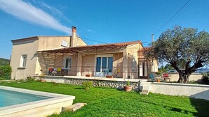 Una casa de dos pisos con piscina, un muro de piedra y un árbol en el jardín.