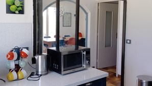Una cocina con microondas, hervidor y soporte para tazas.