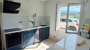 Una cocina moderna con una isla grande, horno empotrado y ventana con vista a un coche aparcado y al paisaje.