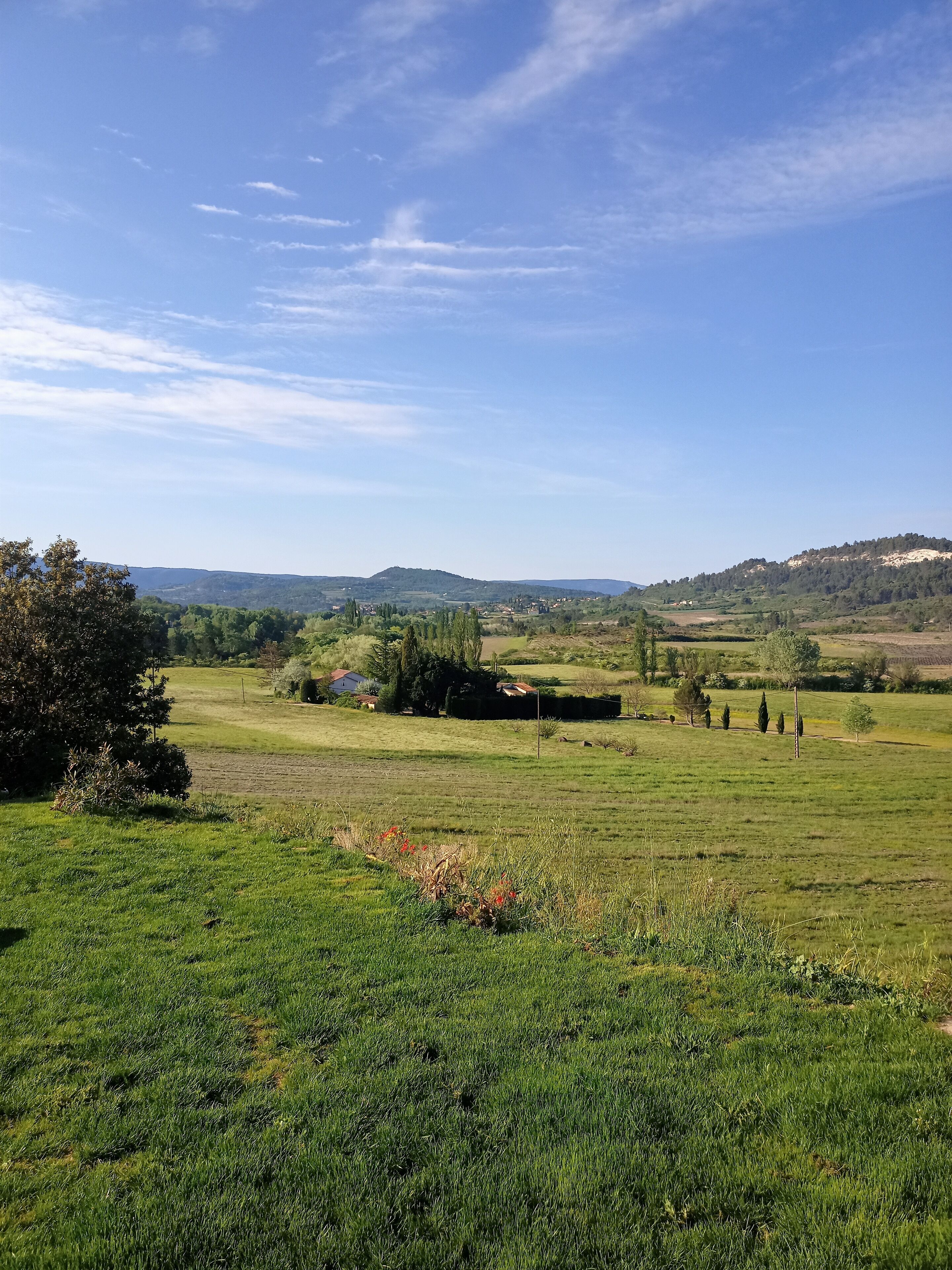 A rural landscape with a clear sky, green fields, and distant hills.