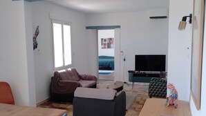 Una sala de estar moderna con una mesa de comedor de madera, un sofá, un televisor y una mesita de noche con una lámpara.