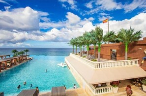 Ein Pool eines Resorts mit Blick auf den Ozean, Palmen und einer Flagge.