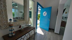 A hallway with a blue door, a wooden console table with decorative items, a stone wall, and a large mirror. - VILLA BEACH HAPPY (Sosúa)