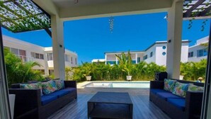 A covered outdoor area with two wicker sofas, a central coffee table, and a pool in the background. - VILLA BEACH HAPPY (Sosúa)