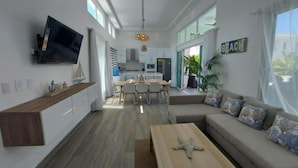 A modern living room with a sofa, coffee table, and TV. - VILLA BEACH HAPPY (Sosúa)