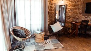 A cozy room with a brick wall, a wicker chair, a small round table, and a mirror.