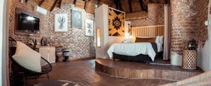 Ein rustikaler Raum mit Backsteinwand, einem Bett mit weißer Bettdecke, einem an der Wand montierten Fernseher und Holzboden.