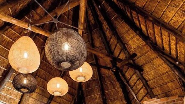 A rustic bedroom with a thatched ceiling, a bed with white bedding, and a decorative wall panel.