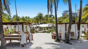 Um resort à beira-mar com cabanas de madeira e toldos brancos, palmeiras e um céu claro.