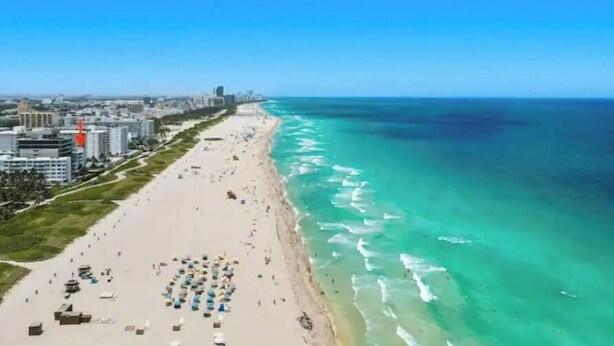 Paisagem costeira com uma praia extensa, céu azul límpido e edifícios ao longo da orla.