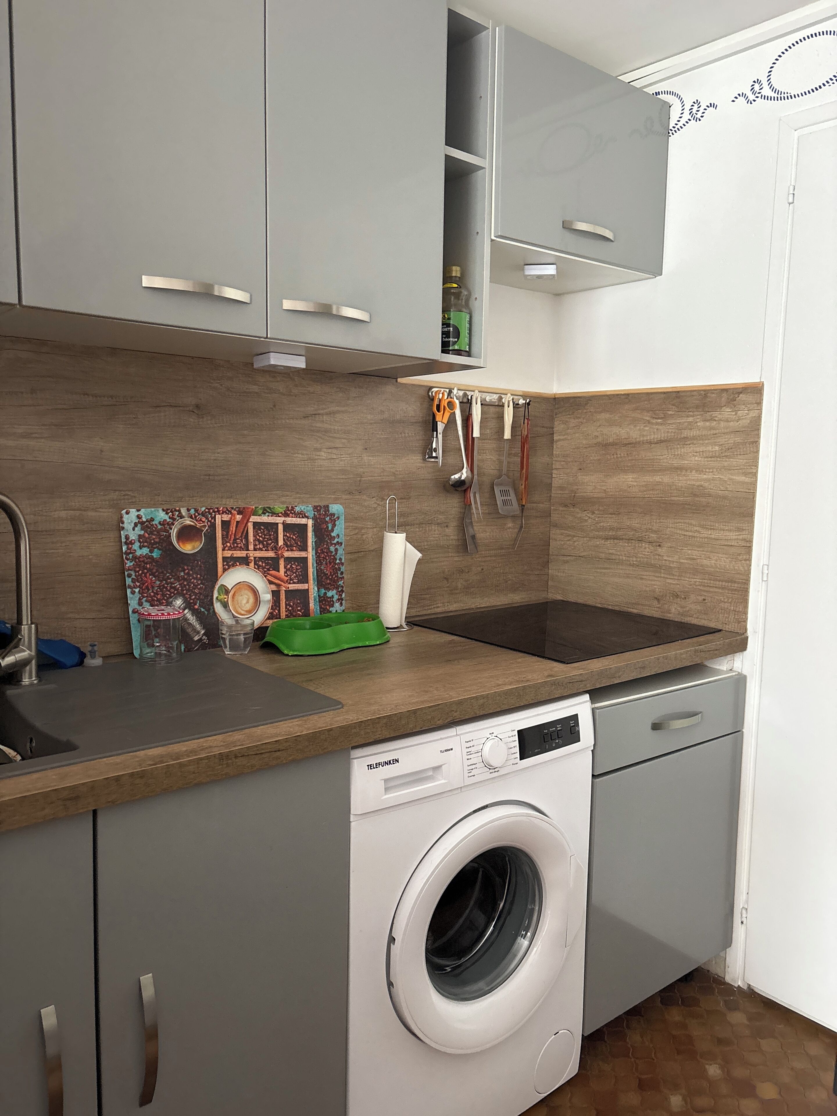 A compact kitchen with a built-in washing machine, a wooden countertop, and a backsplash.