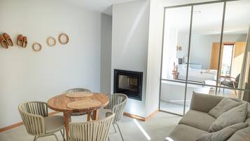 A modern living room with a round wooden table, wicker chairs, a sofa, and a fireplace.