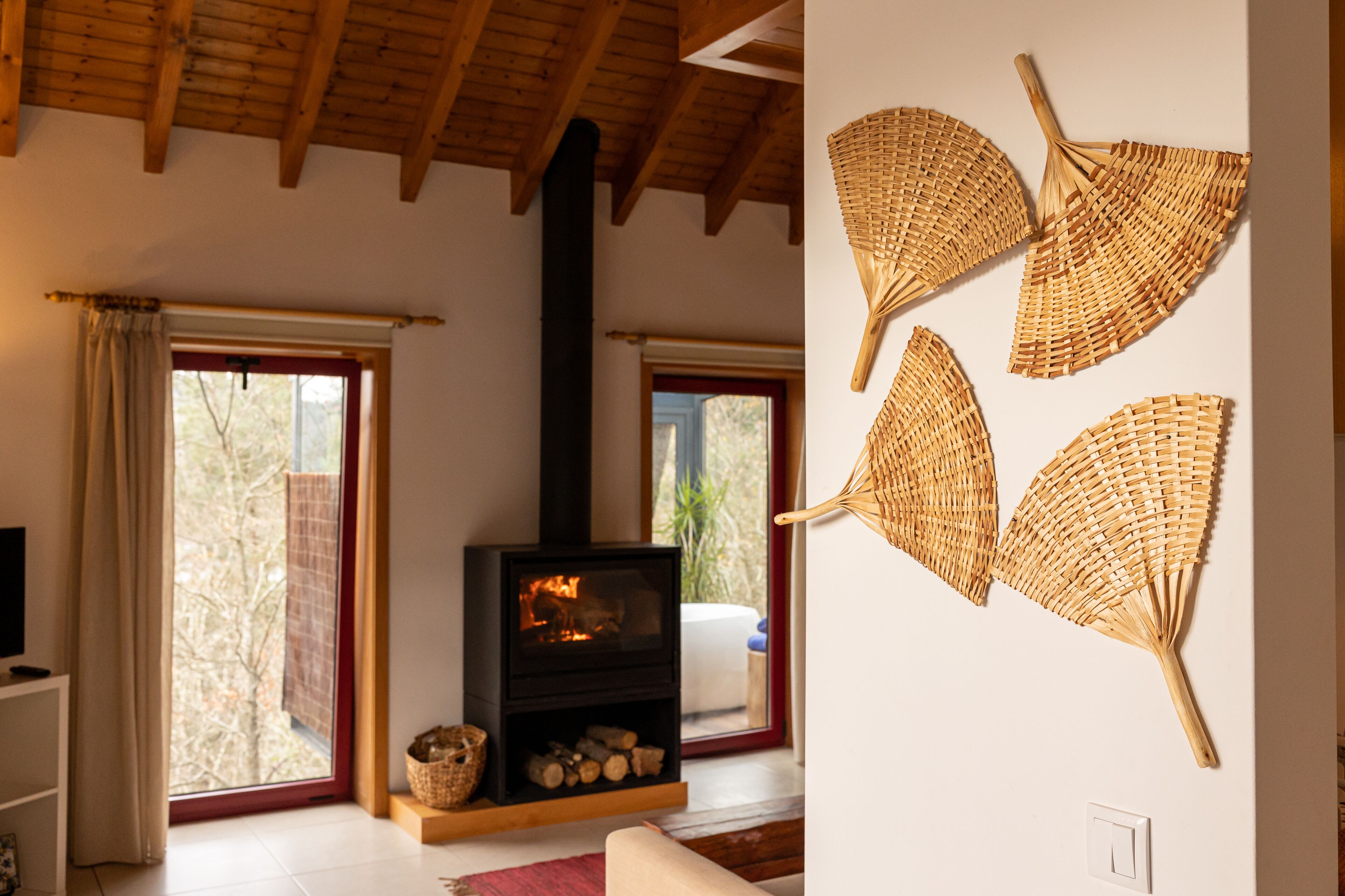 A cozy living room with a fireplace, large windows, and a wall-mounted fan.